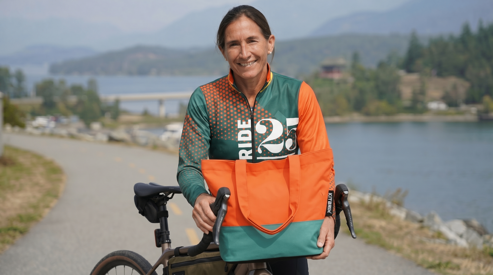 Ride25 rider smiling with bike and Kitbrix tote bag beside a lake in Azerbaijan