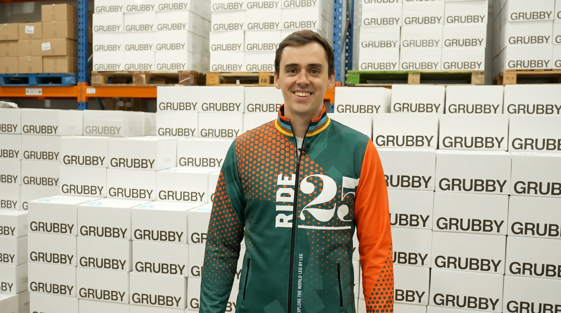 Ride25 rider in a Ride25 jersey standing in front of stacked Grubby boxes in a Staffordshire warehouse