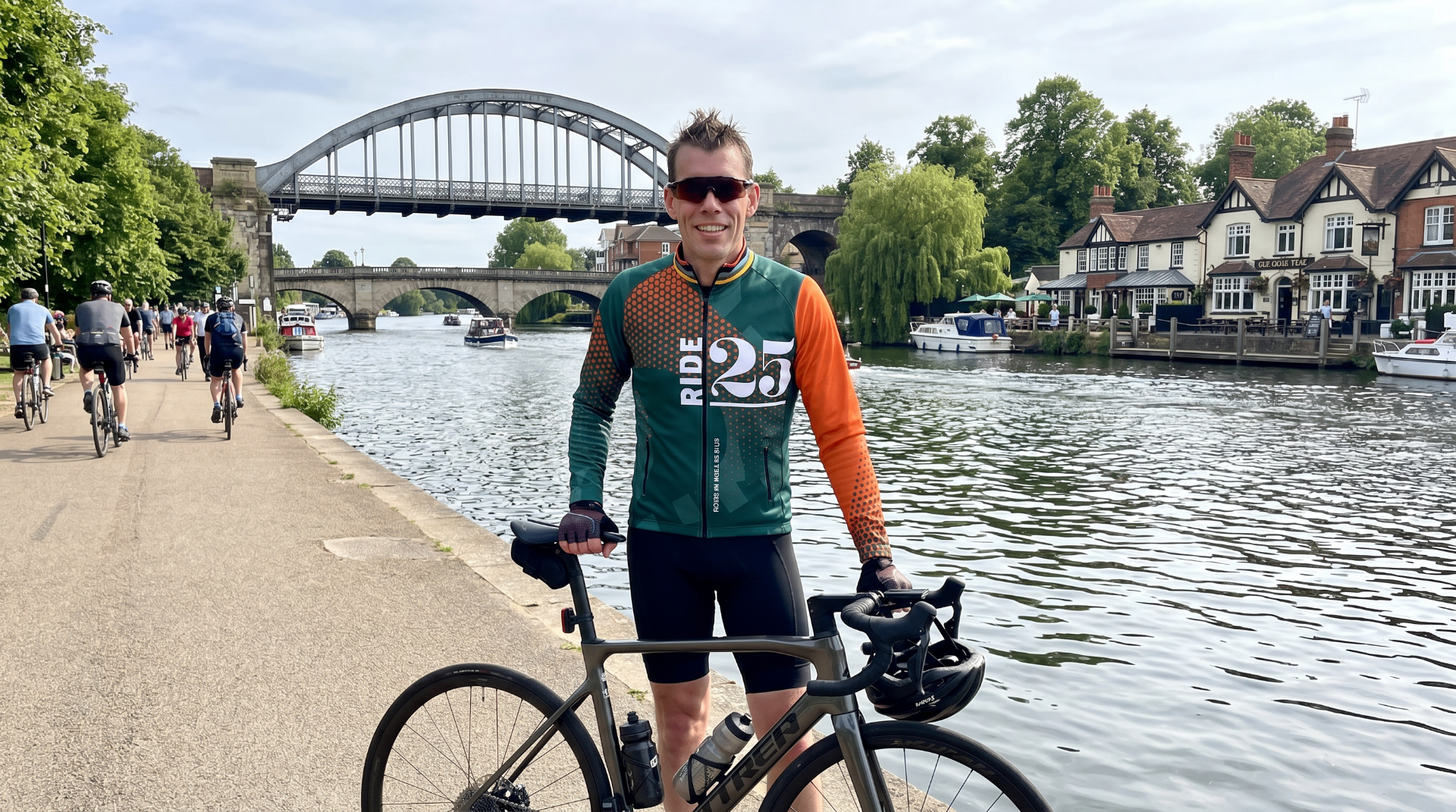 Ride25 rider with bike beside the Thames in Maidenhead in front of a bridge and riverside pub